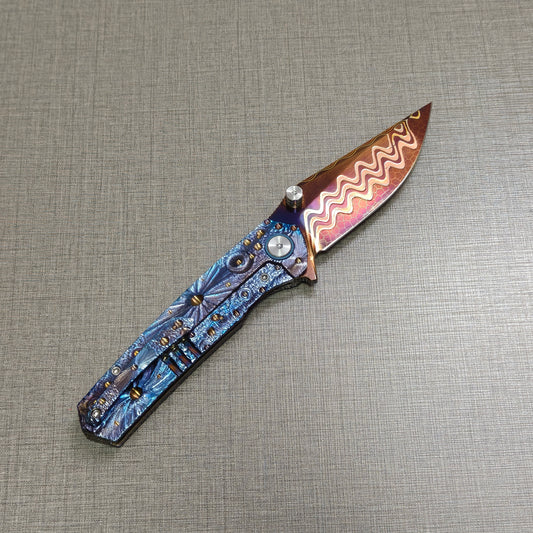 Impact Origin titanium folding knife open, clip side view with hand-flame Damascus blade angled upward