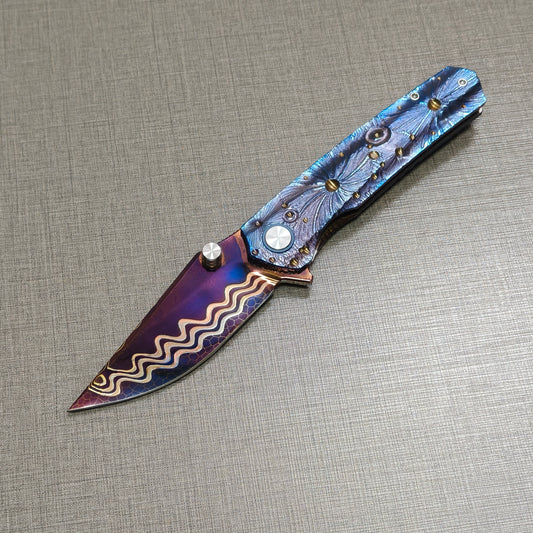 Impact Origin folding knife open, non-clip side showing engraved titanium handle inspired by meteor craters, hand-flamed damascus blade