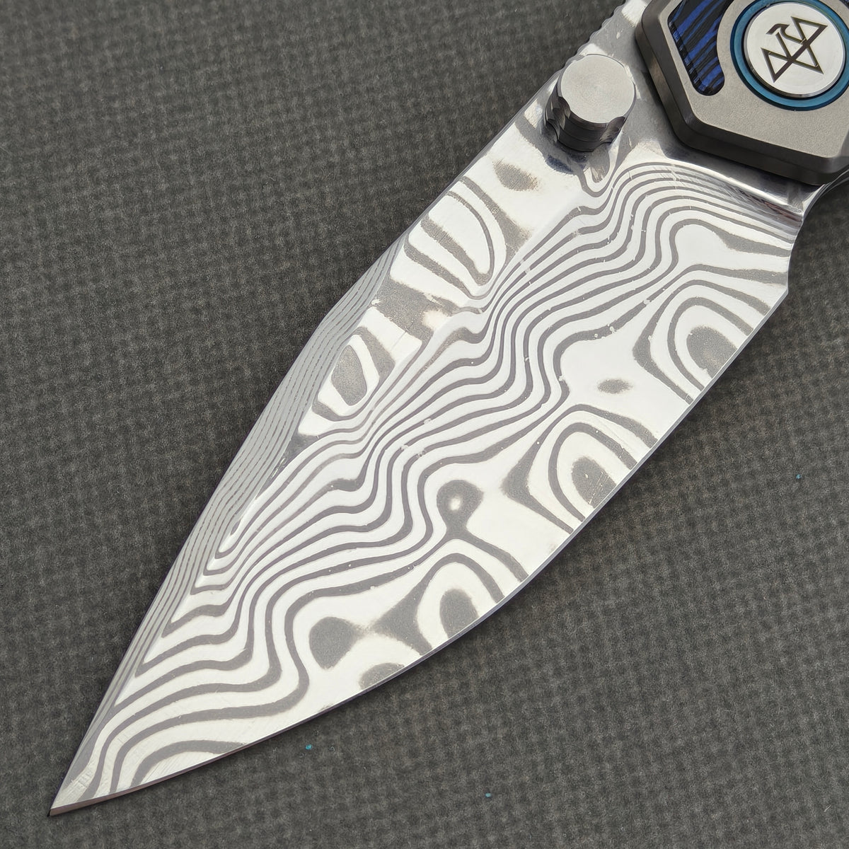 VORIXN Tidecipher KB157 Folding Knife – blade detail showing flowing Damascus patterns, cutting edge, and thumb stud.