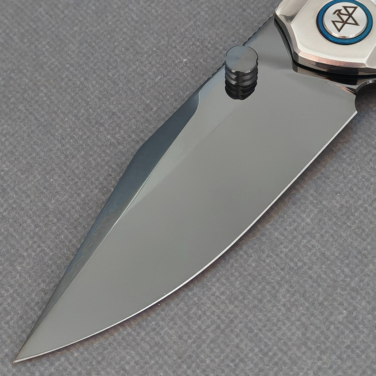 Close-up of the VORIXN Ocean Mirage KB093 dark blade, black thumb stud and logo pivot with a blue ring.
