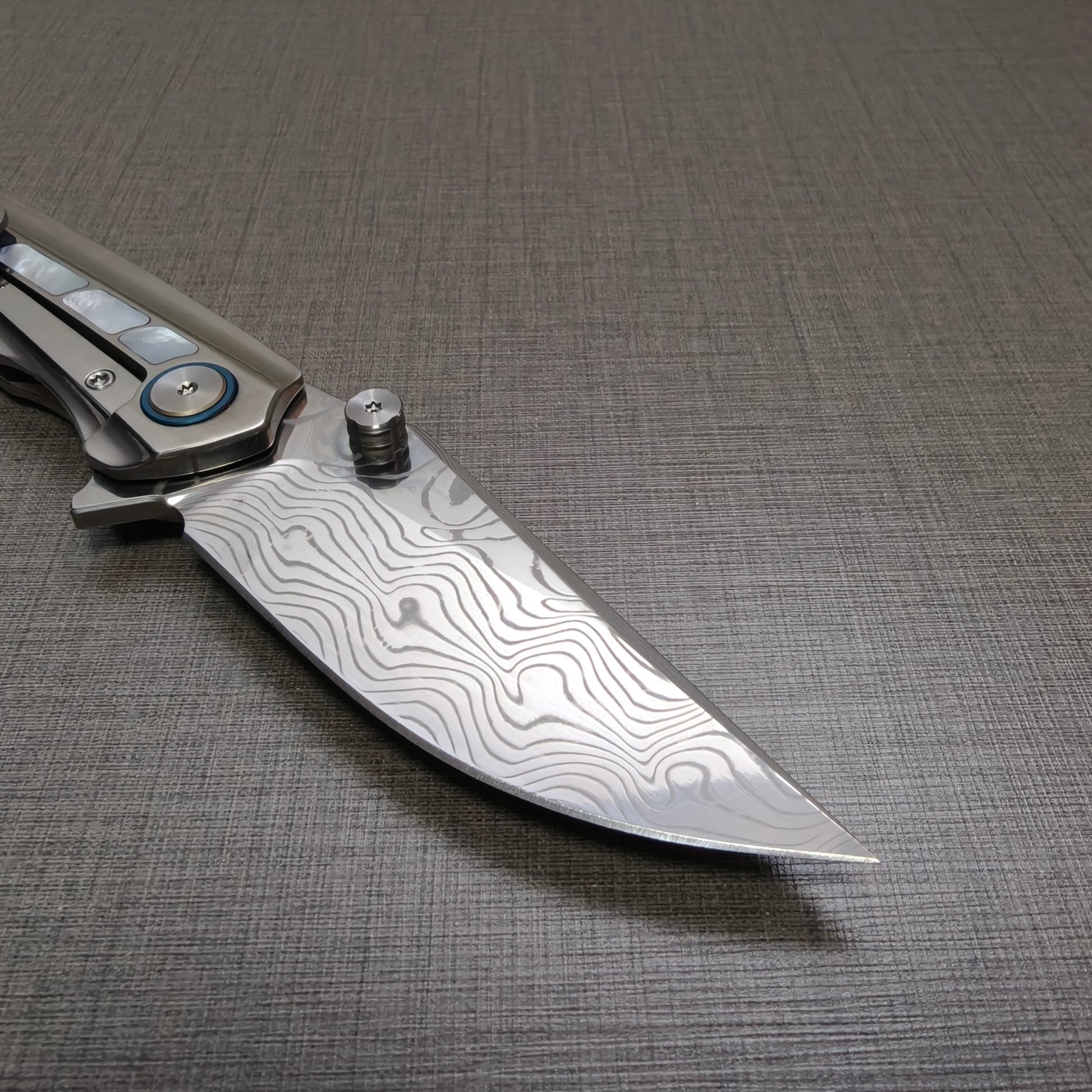 Close-up detail of the VORIXN Ocean Mirage Damascus steel blade showing layered pattern and fine finish