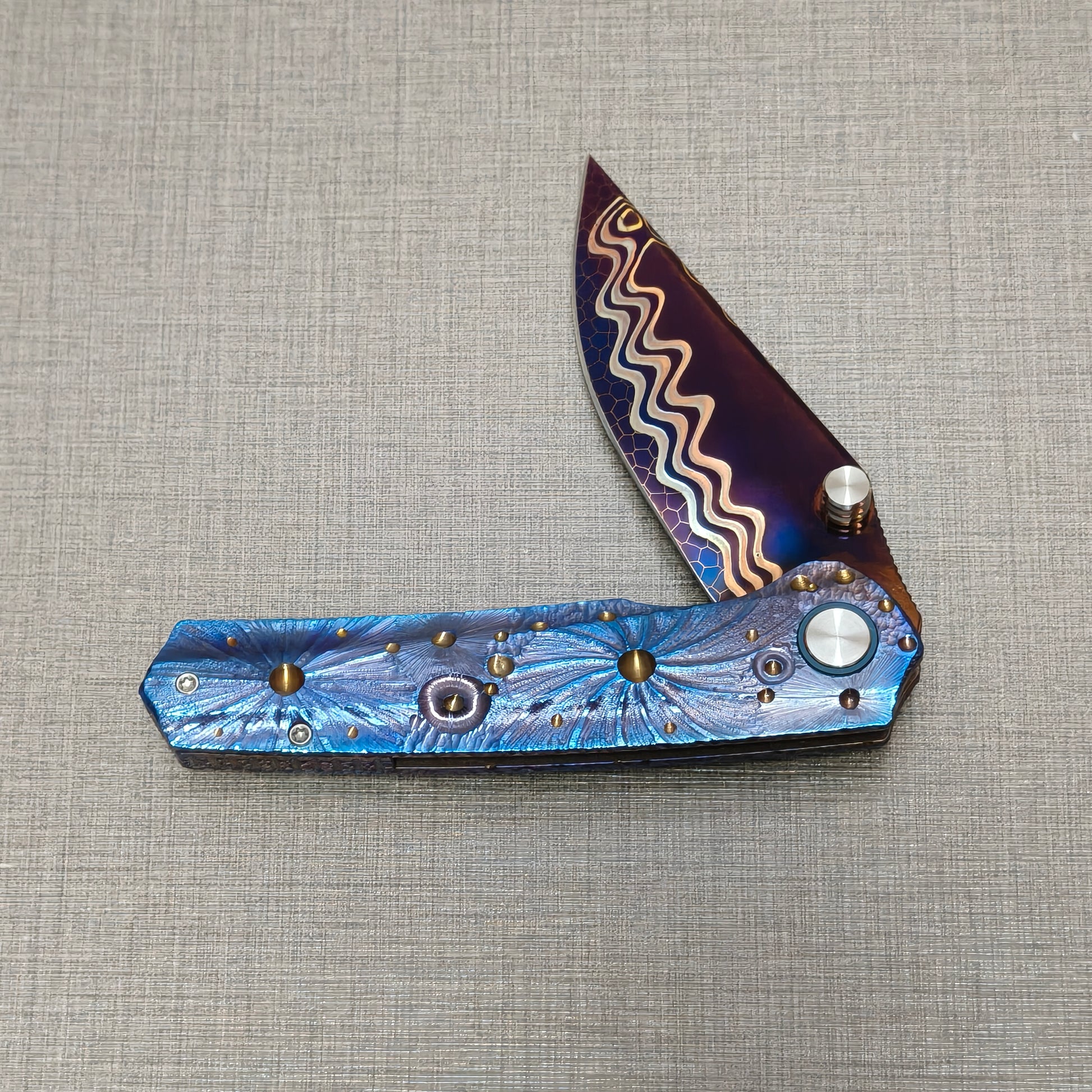 Impact Origin folding knife partially open, highlighting engraved titanium handle texture and planetary surface pattern