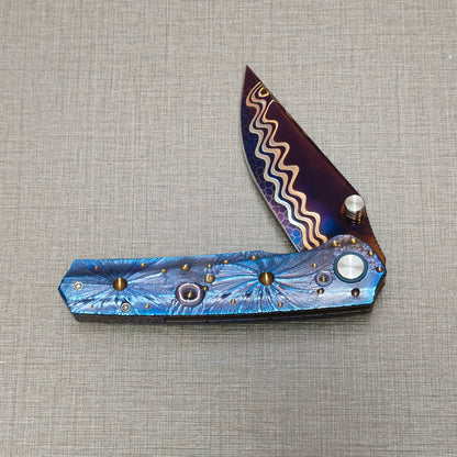 Impact Origin folding knife partially open, highlighting engraved titanium handle texture and planetary surface pattern