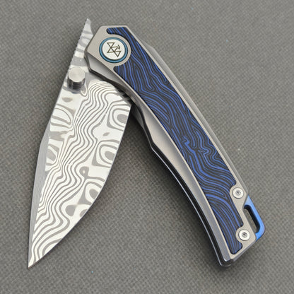 VORIXN Tidecipher KB157 Folding Knife – partially open view showing Damascus blade, thumb stud, and blue wave-pattern inlay.