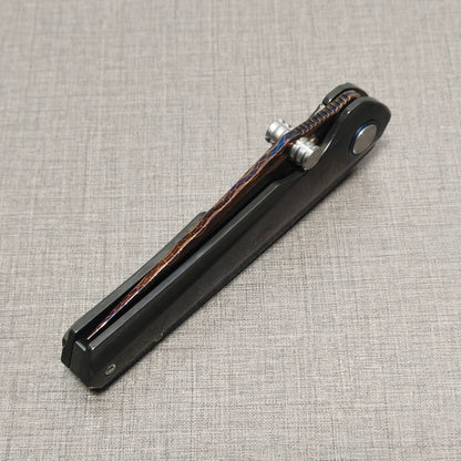 Closed VORIXN Pyretic folding knife shown at an angled view, with the Damascus steel blade positioned on top and the zirconium handle visible